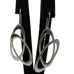 May include: A pair of silver-toned earrings featuring two interlocking, smooth, oval-shaped loops that create an open, abstract design. Each earring is suspended from a simple, curved silver-toned hook wire, showcasing a polished, reflective metallic finish.