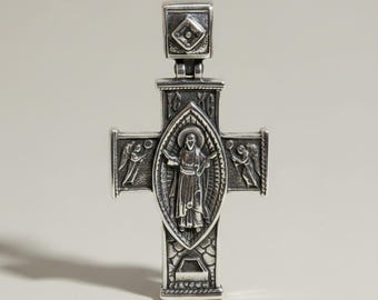 May include: A silver-toned metal cross pendant featuring an embossed central figure of a person with a halo, flanked by two winged figures. The cross includes the engraved text IC XC and has a rectangular bail at the top with a diamond-shaped detail.