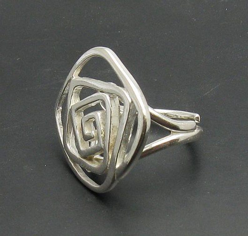May include: A silver ring with a geometric design of overlapping squares. The ring is made of a smooth, polished metal and has a modern, minimalist style.
