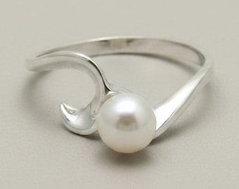 May include: A silver ring featuring a single round white pearl set within a polished metal band. The band curves into a wave-like shape that partially wraps around the pearl, creating a smooth, continuous design with a reflective metallic finish.