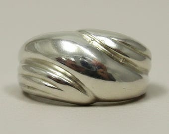 May include: A polished silver ring featuring a wide, domed band with a smooth, reflective surface. The design includes a series of diagonal, recessed grooves that create a layered, overlapping appearance across the front of the metal band.