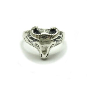 Peut inclure: Une bague en métal argenté représentant une tête de bélier sculptée. La surface de la bague présente des gravures détaillées pour représenter la texture de la fourrure et des cornes incurvées du bélier, avec des zones sombres en relief.