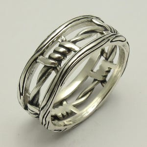 May include: A polished silver ring featuring a continuous band design that mimics the appearance of twisted barbed wire. The metal has a bright, reflective finish with darkened recessed areas that emphasize the sharp, coiled wire details.