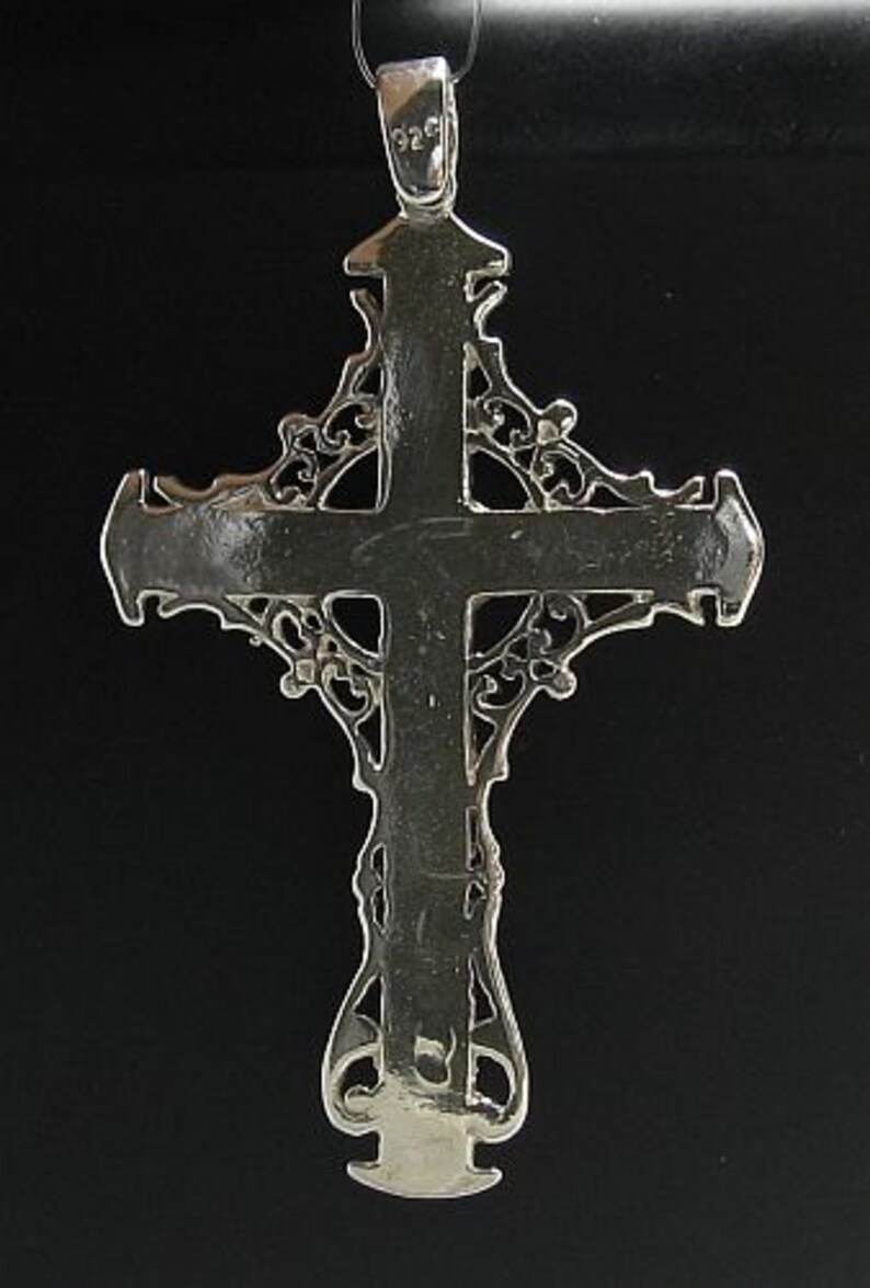 May include: A silver filigree cross pendant with a detailed design. The cross is marked with "925" on the top.