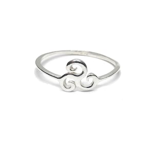 May include: A polished sterling silver ring featuring a central triskelion motif. The band is thin and circular, with the three-armed spiral design integrated into the front. The metal has a bright, reflective finish and the hallmark 925 is visible.