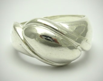 Puede incluir: Un anillo de plata pulida con una banda ancha y lisa que presenta un diseño retorcido, continuo y superpuesto, creando una forma redondeada y voluminosa. La superficie metálica es altamente reflectante, mostrando brillos y sombras suaves.