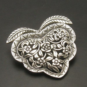 May include: A silver heart-shaped pendant featuring an intricate floral design. The pendant is crafted from delicate filigree work and showcases a beautiful floral pattern.