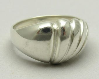 Könnte beinhalten: Ein polierter Silberring mit einer glatten, abgerundeten Ringschiene, die in ein erhabenes, fächerartiges Design übergeht. Der obere Teil des Rings zeigt eine Reihe von vier ausgeprägten, geschwungenen, vertikalen Rippen mit muschelartiger Struktur.