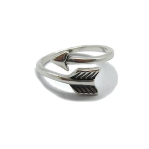 May include: A silver ring with a double arrow design. The arrow is pointing to the right and is wrapped around the band of the ring.