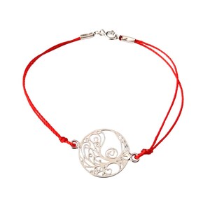 Può includere: Un bracciale in cordino rosso con un ciondolo circolare color argento caratterizzato da un intricato motivo a filigrana traforato. Il bracciale è fissato con una chiusura a moschettone in metallo e un anellino che unisce i capi del cordino.