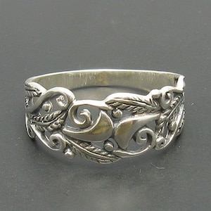 Puede incluir: Un anillo de plata con un delicado y complejo diseño de hojas y enredaderas en espiral.