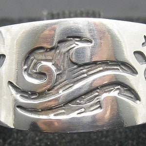 May include: A silver ring featuring a wave design and two stylised lizards on either side.