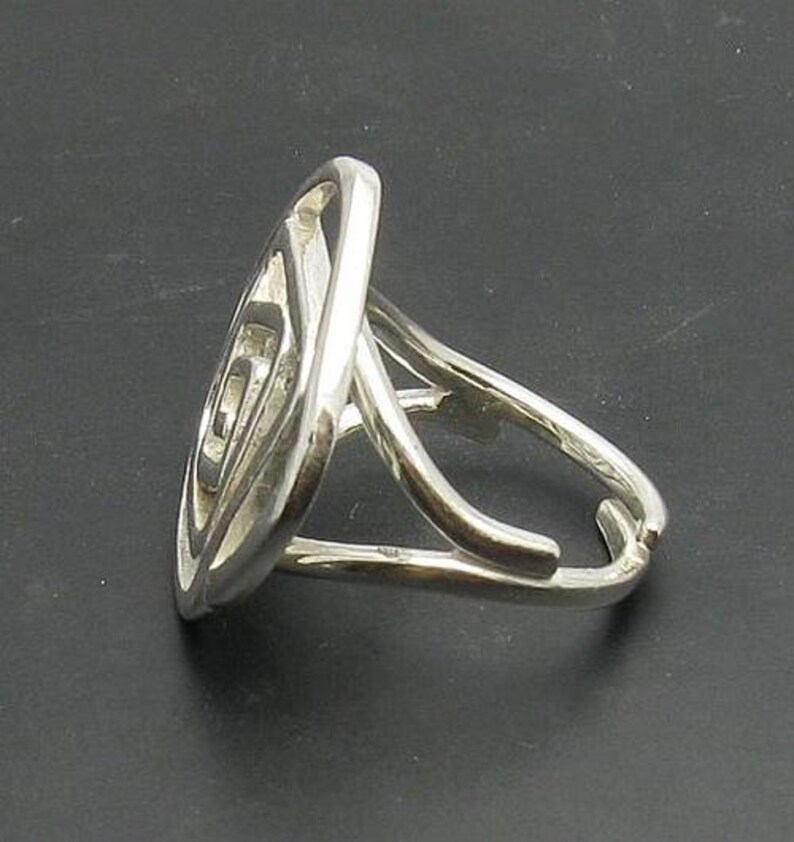 May include: A silver ring with a unique, abstract design. The ring is made of a single piece of metal that is twisted and turned to create a complex pattern.