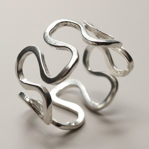 May include: A silver ring featuring a continuous, fluid, and wavy wire design that forms an open, interconnected structure. The metal has a polished, reflective surface with smooth, rounded edges throughout the entire band construction.