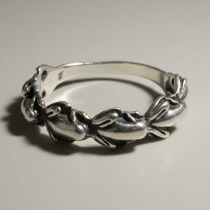May include: A silver ring featuring a continuous band of sculpted, repeating rabbit figures. The metal has a polished finish with darkened recessed areas to highlight the detailed shapes of the small animals encircling the entire circumference of the band.