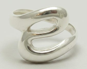 Könnte beinhalten: Ein polierter Silberring mit einem durchgehenden, fließenden und offenen Design, das eine stilisierte, abgerundete Form bildet. Die Metalloberfläche ist glatt und reflektierend und erzeugt eine nahtlose Schleife, die den Finger mit einem glänzenden Finish umschließt.