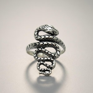 May include: A silver-toned metal ring shaped like a coiled snake. The design features intricate scale textures along the body of the serpent, with the head positioned at the top and the tail curving downward to form the band of the ring.