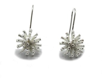 May include: A pair of silver drop earrings featuring a spherical, starburst-like design composed of numerous thin, radiating metal rods with rounded tips. Each earring is attached to a simple, curved silver hook for hanging from the earlobe.