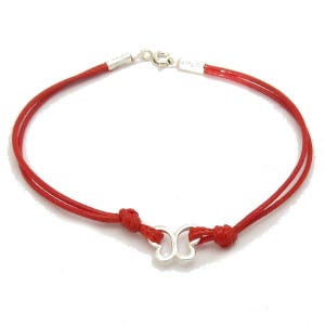 May include: A red cord bracelet featuring a silver-toned butterfly charm at the center. The bracelet is constructed from two strands of red cord, each knotted to secure the central butterfly charm, and finished with a silver-toned metal clasp.