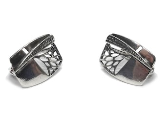 May include: A pair of silver-toned earrings featuring a rectangular shape with a curved edge. Each earring displays a polished metallic surface on one side and an intricate, openwork lattice pattern on the other, separated by a textured diagonal bar.