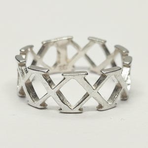 May include: A silver-toned ring featuring a continuous openwork design composed of repeating X-shaped motifs. The band has a polished metallic finish and a uniform structure throughout, with the number 925 clearly stamped on the inner surface.