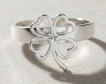 Op de afbeelding: Een ring van gepolijst zilver met een opvallend uitgesneden klavertjevier-ontwerp in het midden van de band. Het klavermotief is opengewerkt met gladde, afgeronde randen en het metaal heeft over het gehele sieraad een reflecterende afwerking.