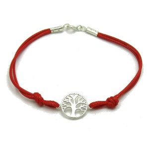 Puede incluir: Pulsera de cordón rojo con un colgante de árbol de la vida plateado. La pulsera tiene un cierre de nudo corredizo y detalles metálicos plateados. El colgante del árbol de la vida es de diseño circular.