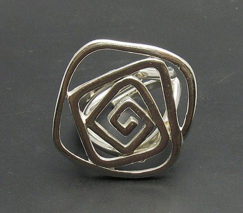 May include: Silver ring with a geometric design featuring multiple overlapping squares.