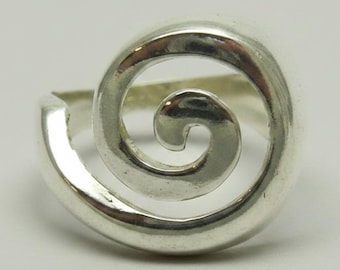 May include: A polished silver ring featuring a prominent spiral design that curves inward to a central point. The band is smooth and reflective, showcasing a continuous metallic loop that forms a circular shape on the front of the jewelry piece.