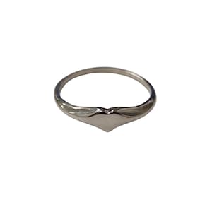 Puede incluir: Un anillo plateado con un diseño en forma de corazón. El anillo está hecho de un material metálico brillante y presenta un acabado liso y pulido. La forma de corazón está centrada en la banda del anillo.