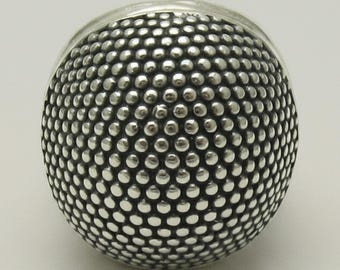 May include: A silver thimble featuring a rounded top covered in a dense, uniform pattern of small, raised circular indentations. The metallic surface has a polished finish with dark oxidation within the recessed areas between the dots.