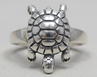 May include: A silver ring featuring a three-dimensional turtle design on the front. The turtle shell has a segmented, rounded pattern with oxidized detailing in the grooves, while the head and four legs extend from the central shell element.