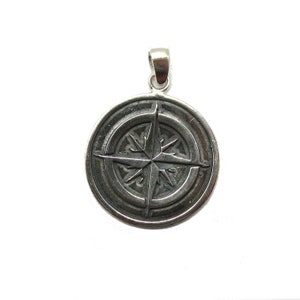 May include: A silver compass pendant with a detailed star design. The pendant is round and has a smooth, polished finish.