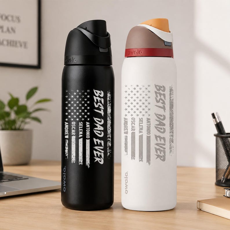 Puede incluir: Dos botellas de agua aisladas, una negra y otra blanca, con tapas negras. Cada botella presenta un dise&ntilde;o de bandera estadounidense desgastada y el texto "BEST DAD EVER" con nombres debajo. Las botellas est&aacute;n sobre un escritorio de madera.