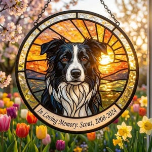 May include: Stained glass memorial featuring a black and white Border Collie with a sunset backdrop. The circular design includes the text "In Loving Memory: Scout, 2008-2024" and is suspended by a chain. The image is set against a background of colorful flowers.