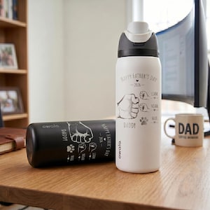 May include: Two insulated water bottles, one black and one white, with a flip-top lid. The white bottle has "Happy Father's Day - 2026" and "Daddy" printed on it, along with fist and paw print graphics. The black bottle has similar text and graphics.