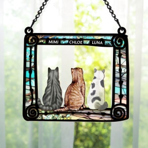 May include: A stained glass window hanging with three cats sitting in a row. The cats are facing away from the viewer. The names Mimi, Chloe, and Luna are written above the cats.