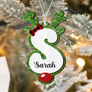 May include: Green glitter reindeer ornament with a red and black plaid bow and a white letter S with the name "Sarah" written on it. The ornament has a red nose.