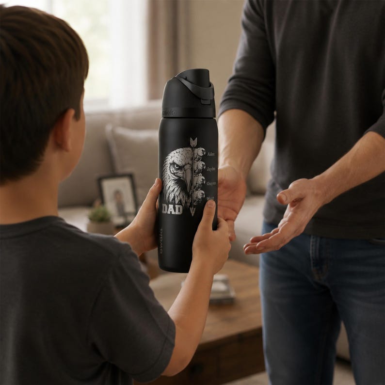 May include: A black water bottle with a silver eagle design and the word "DAD" printed on it. The bottle is being held by a child and offered to an adult. The bottle has a black lid and a silver arrow design.