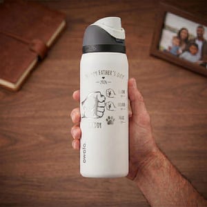 May include: A white Owala water bottle with a gray lid. The bottle has the text "Happy Father's Day - 2026" and a graphic of a fist, three smaller fists, and paw prints. The names Liam, Noah, and Max are below the smaller fists.