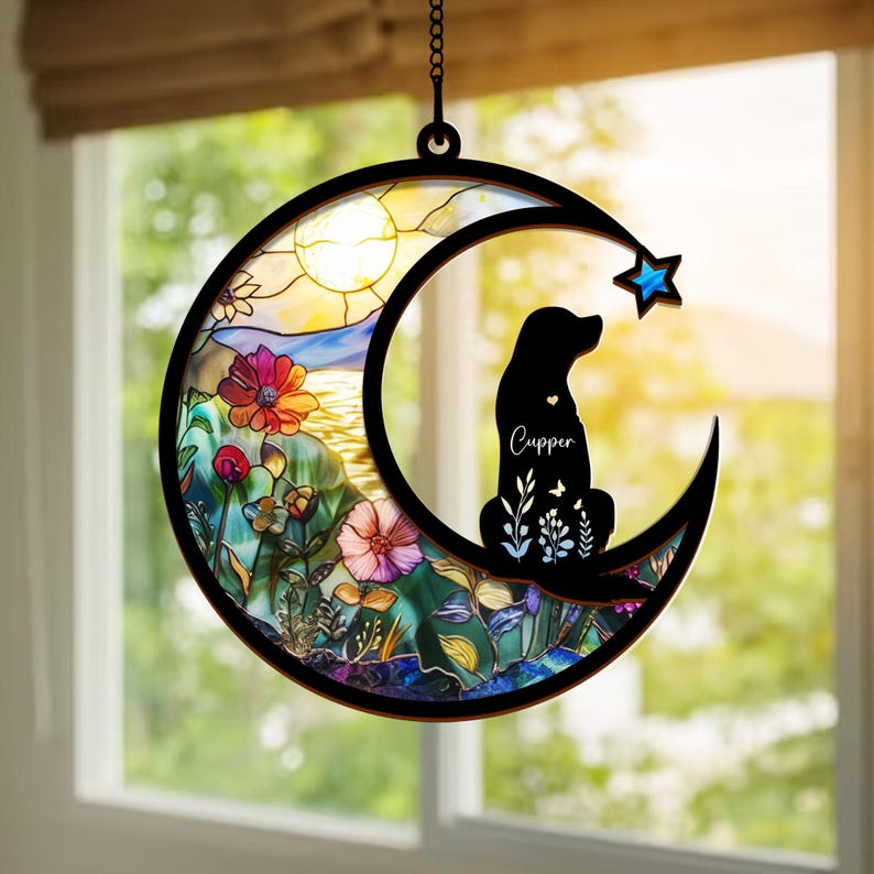 Puede incluir: Un atrapasol de vidrio tintado en forma de media luna con una silueta de un perro sentado en su interior. La luna est&aacute; rodeada de flores coloridas y una escena de puesta de sol. El nombre del perro, "Cupper", est&aacute; escrito debajo de la silueta.