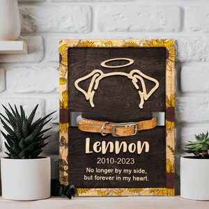 May include: A wooden memorial plaque with a sunflower border, a dog silhouette with a halo, a collar, and the text "Lennon 2010-2023 No longer by my side, but forever in my heart."