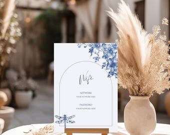 May include: A white sign on a wooden easel with blue floral accents and the word "Wifi". The sign includes fields for network and password information, and a dragonfly illustration. A vase of dried flowers sits nearby.