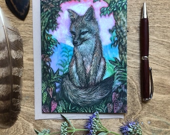 May include: A greeting card featuring a detailed illustration of a fox in a forest setting, with a pen, a feather, a wooden heart, and flowers. The fox is depicted with gray and brown fur, surrounded by lush green foliage and a colorful sky.