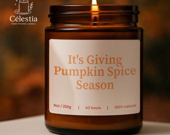 May include: A lit, brown glass jar candle with the text "It's Giving Pumpkin Spice Season" on a white label. The candle is 9oz / 255g and burns for 40 hours. The candle is 100% natural.