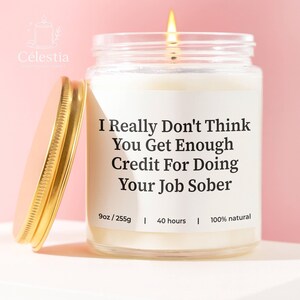 May include: A lit, white candle in a clear glass jar with a gold lid. The label reads "I Really Don't Think You Get Enough Credit For Doing Your Job Sober." The candle is 9oz and burns for 40 hours.