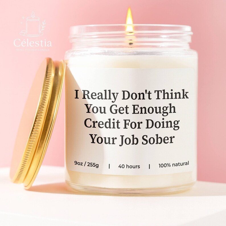 May include: A lit, white candle in a clear glass jar with a gold lid. The label reads "I Really Don't Think You Get Enough Credit For Doing Your Job Sober." The candle is 9oz and burns for 40 hours.