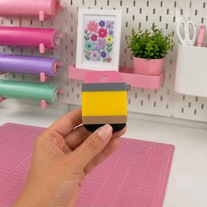 May include: A pencil-shaped silicone case featuring a pink top, a yellow middle section, a tan band, and a black base. The case has a small circular hole at the top for hanging or attachment, designed with a smooth, flat, and rectangular profile.