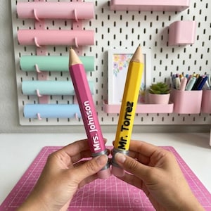 May include: Two large, oversized pencil-shaped items, one in bright pink and one in yellow, each featuring a pointed tip and a flat eraser end. The pink pencil is personalized with the white text Mrs. Johnson, and the yellow pencil features the black text Mr. Torrez.