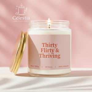 May include: A lit, hand-poured candle in a clear glass jar with a gold lid. The label reads "Thirty Flirty & Thriving." The candle is 9oz/255g and burns for 40 hours. The brand name is Célestia.